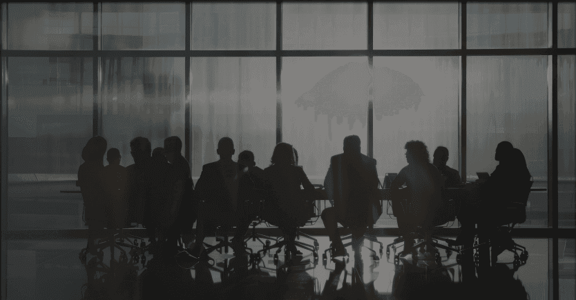 the silhouette of a group of people at a meeting table in a fully glass room