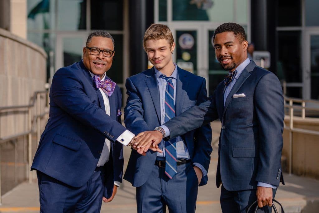 Attorney Arnold Reed, Attorney Arnold Reed II, and a young associate celebrating a victory in the courtroom with a hand stack